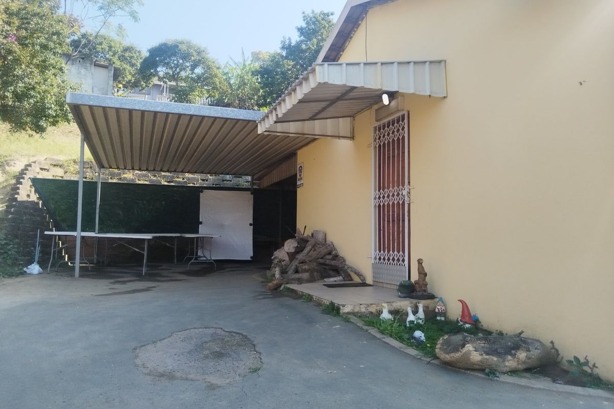 Rear exterior view of the property featuring a metal carport, concrete driveway, and security gate access to the building.
