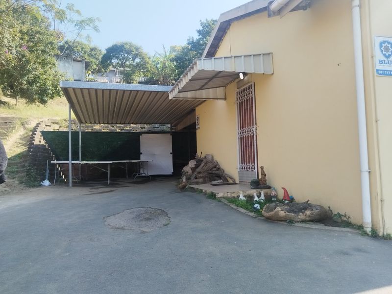 Rear exterior view showing a paved driveway, metal carport structure, and access to the building via a security gate.
