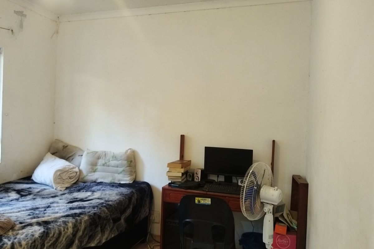 A bedroom featuring tiled flooring and coved ceilings, currently showing signs of wear including peeling paint and wall surface damage.
