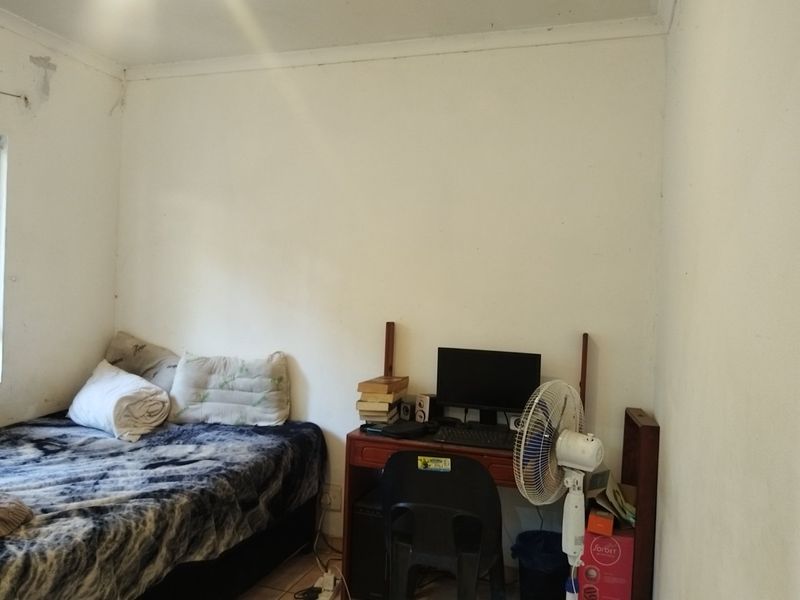 A bedroom featuring tiled flooring and coved ceilings, currently showing signs of wear including peeling paint and wall surface damage.