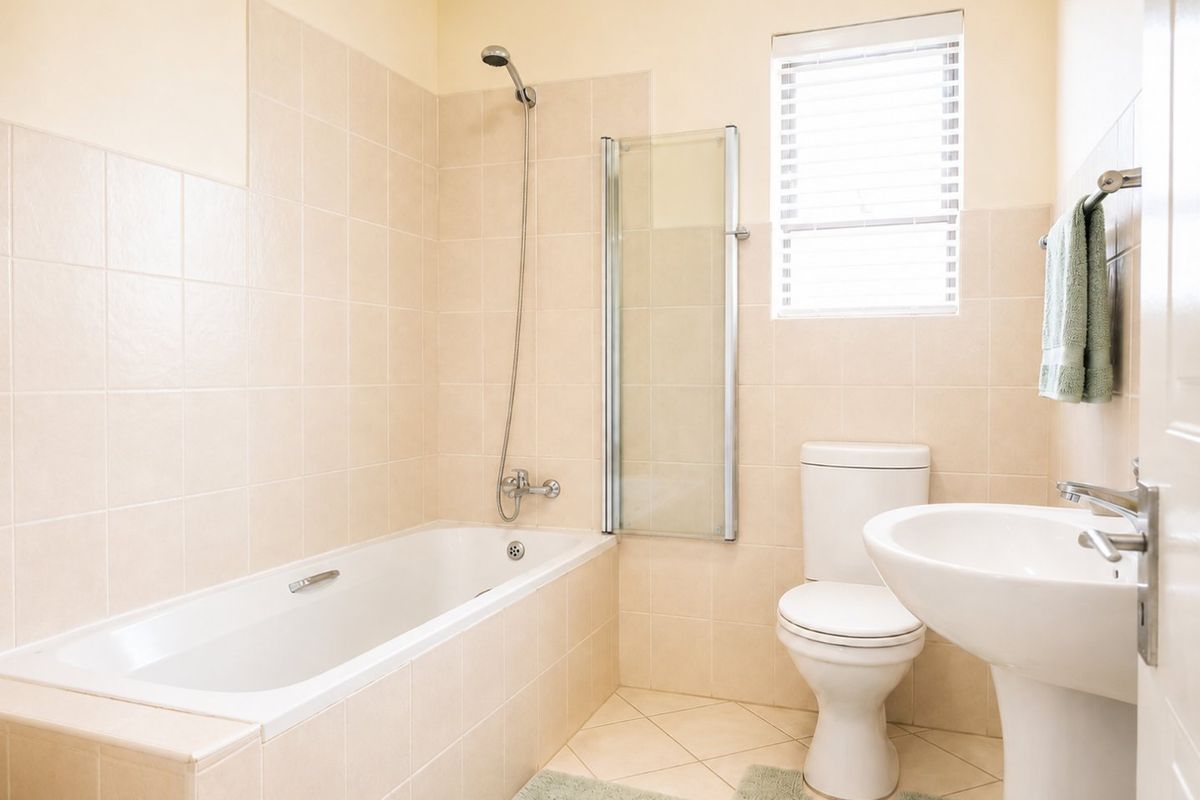 A clean and functional bathroom featuring a bathtub with a shower attachment, glass screen, pedestal basin, and neutral wall tiling.