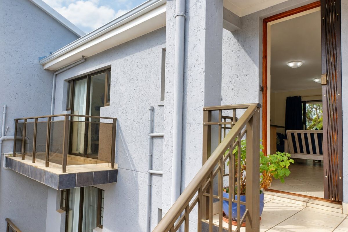 Exterior view of an apartment building featuring a balcony with metal railings, tiled flooring, and sliding glass door access to the interior living space.