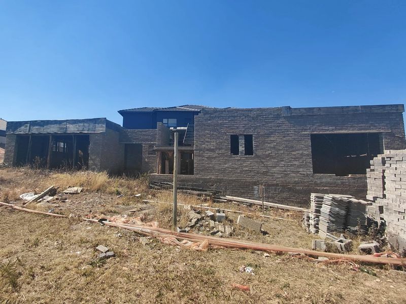 An unfinished residential property under construction, featuring exposed brickwork and structural framing on a vacant plot.