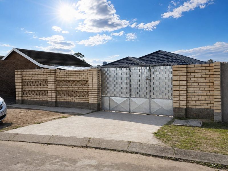 Front view of the property featuring a secure metal driveway gate and a decorative brick boundary wall with a concrete driveway.