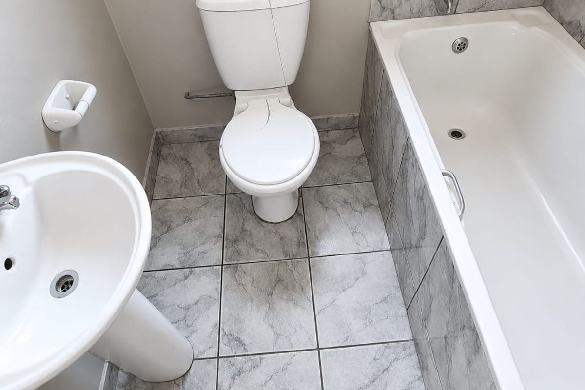 A compact bathroom featuring a pedestal basin, toilet, and bathtub with marble-effect tiled flooring and splashbacks.