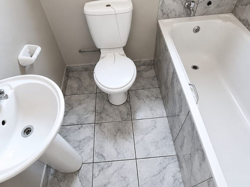 A compact bathroom featuring a pedestal basin, toilet, and bathtub with marble-effect tiled flooring and splashbacks.
