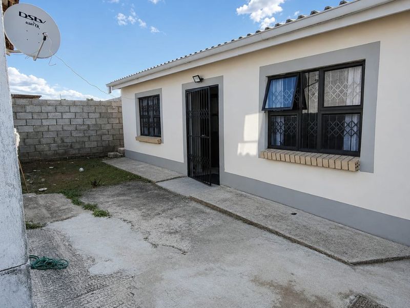 Rear exterior view of the house featuring a concrete patio area, security gates, and a cinder block boundary wall.