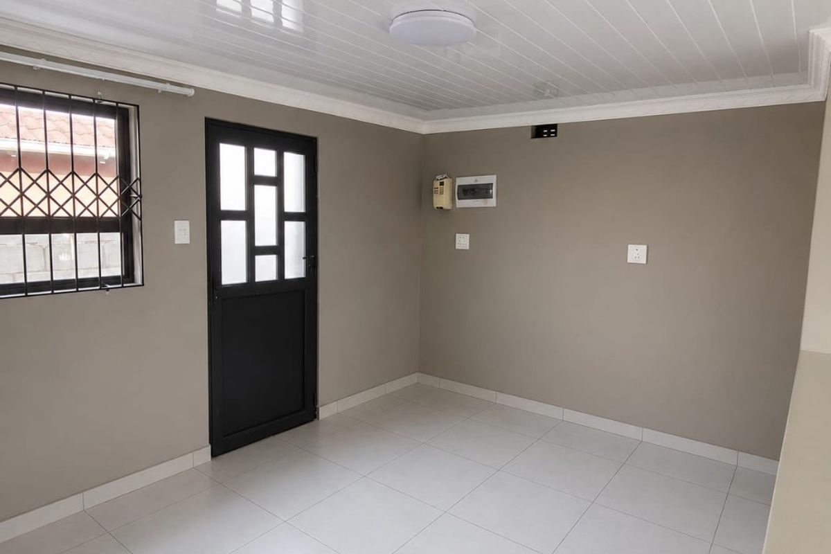 A clean, empty living area featuring neutral wall tones, tiled flooring, a modern PVC ceiling, and secure access via a fitted security gate.