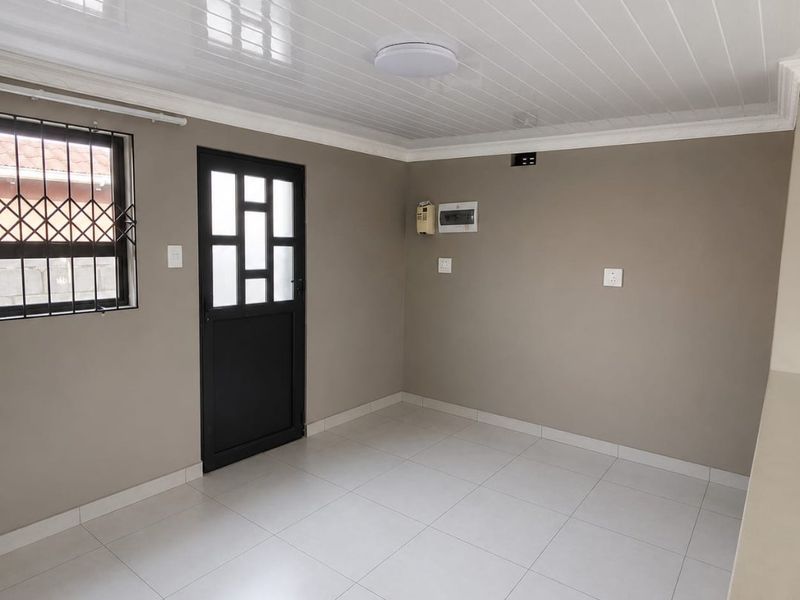 A clean, empty living area featuring neutral wall tones, tiled flooring, a modern PVC ceiling, and secure access via a fitted security gate.