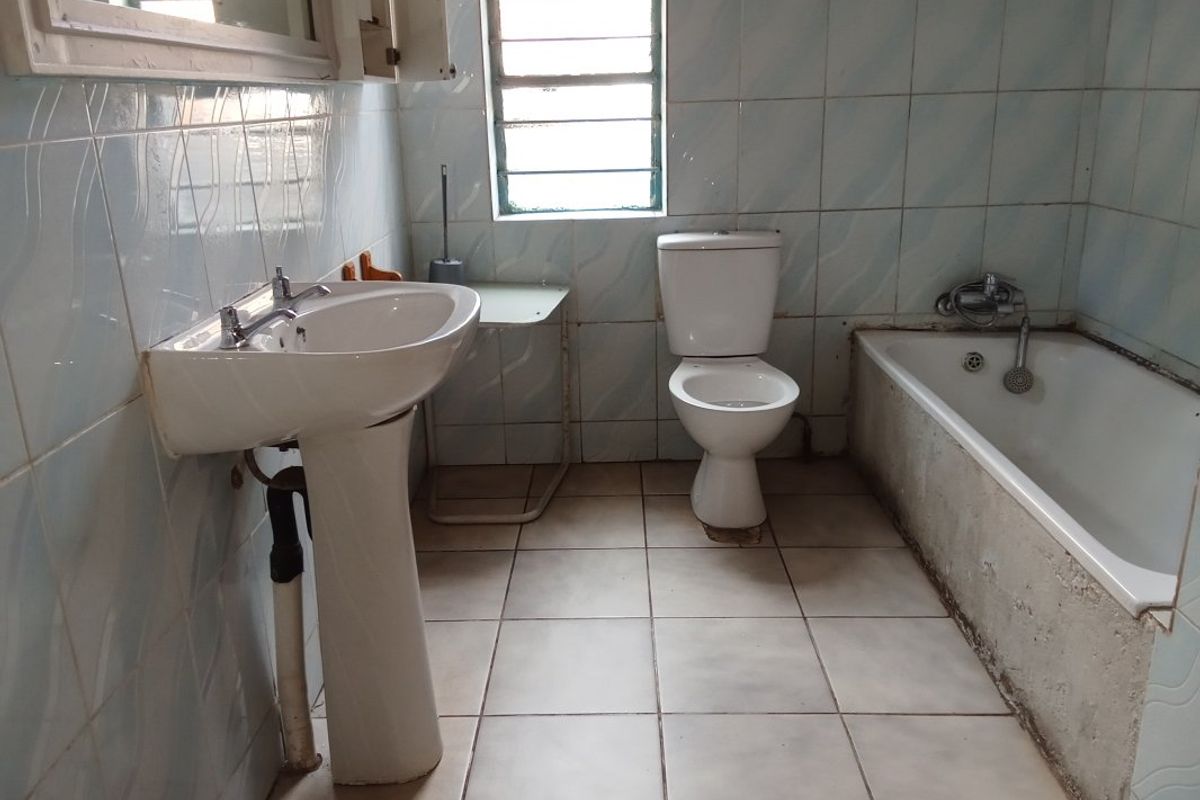 A dated bathroom featuring a pedestal basin, standard toilet, and bathtub with tiled finishes, requiring renovation to modernize the space.