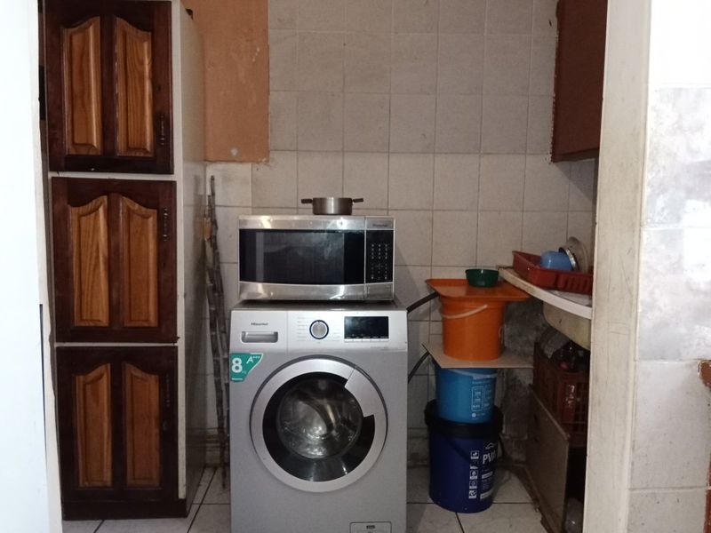 A small laundry area featuring tiled walls and flooring with built-in wooden cabinetry, requiring maintenance and cosmetic updates to improve functionality and appearance.