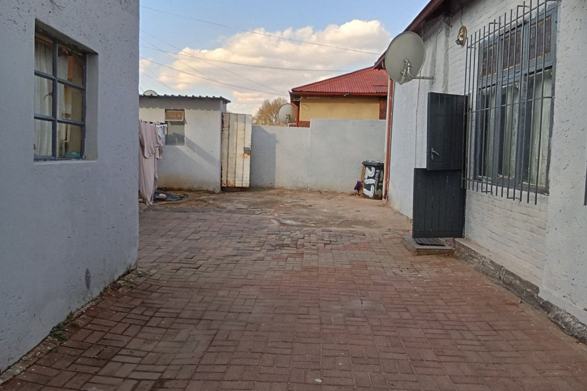 A paved rear courtyard area featuring boundary walls, security bars on windows, and a satellite dish installation.