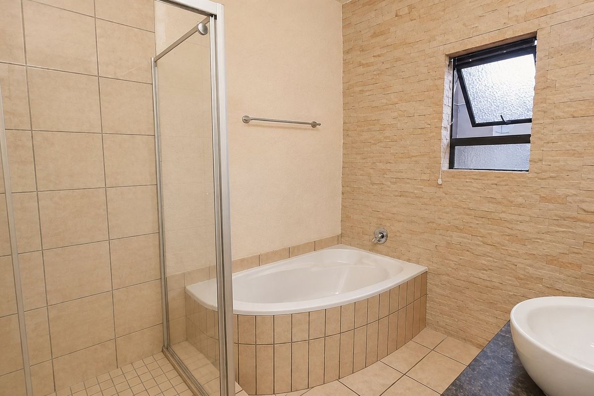 A well-maintained bathroom featuring a built-in bathtub, a separate glass-enclosed shower, and a stone-look feature wall with a top-hung window.