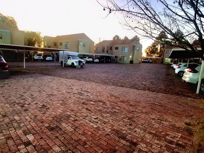 A view of the apartment complex exterior featuring a paved parking area with covered carports and residential building facades.