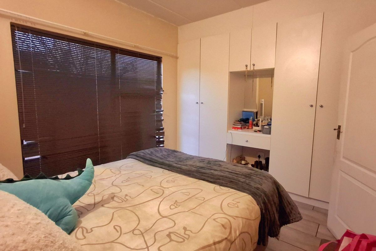 A bedroom featuring built-in cupboards with an integrated vanity unit, tiled flooring, and venetian blinds.