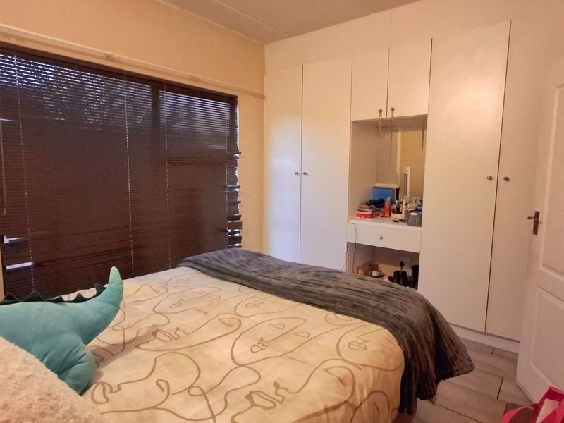 A bedroom featuring built-in cupboards with an integrated vanity unit, tiled flooring, and venetian blinds.