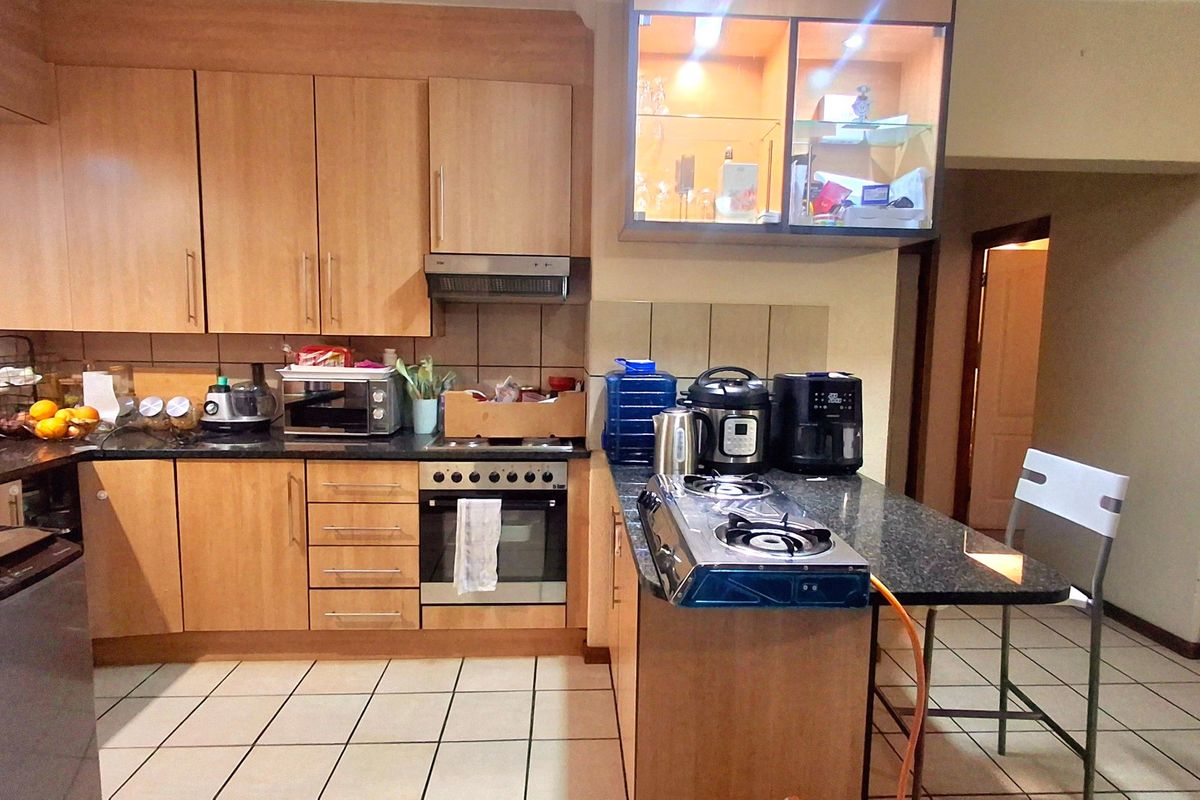 A functional kitchen featuring light wood cabinetry, dark countertops, tiled flooring, and a built-in oven with an extractor fan.