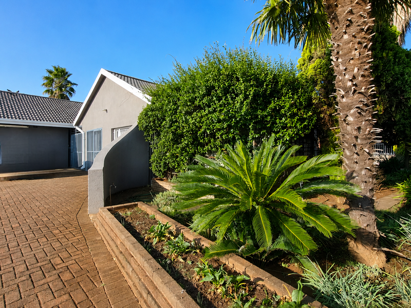 Front exterior view of the house featuring a paved driveway, established garden with a brick planter box, and a well-maintained facade.