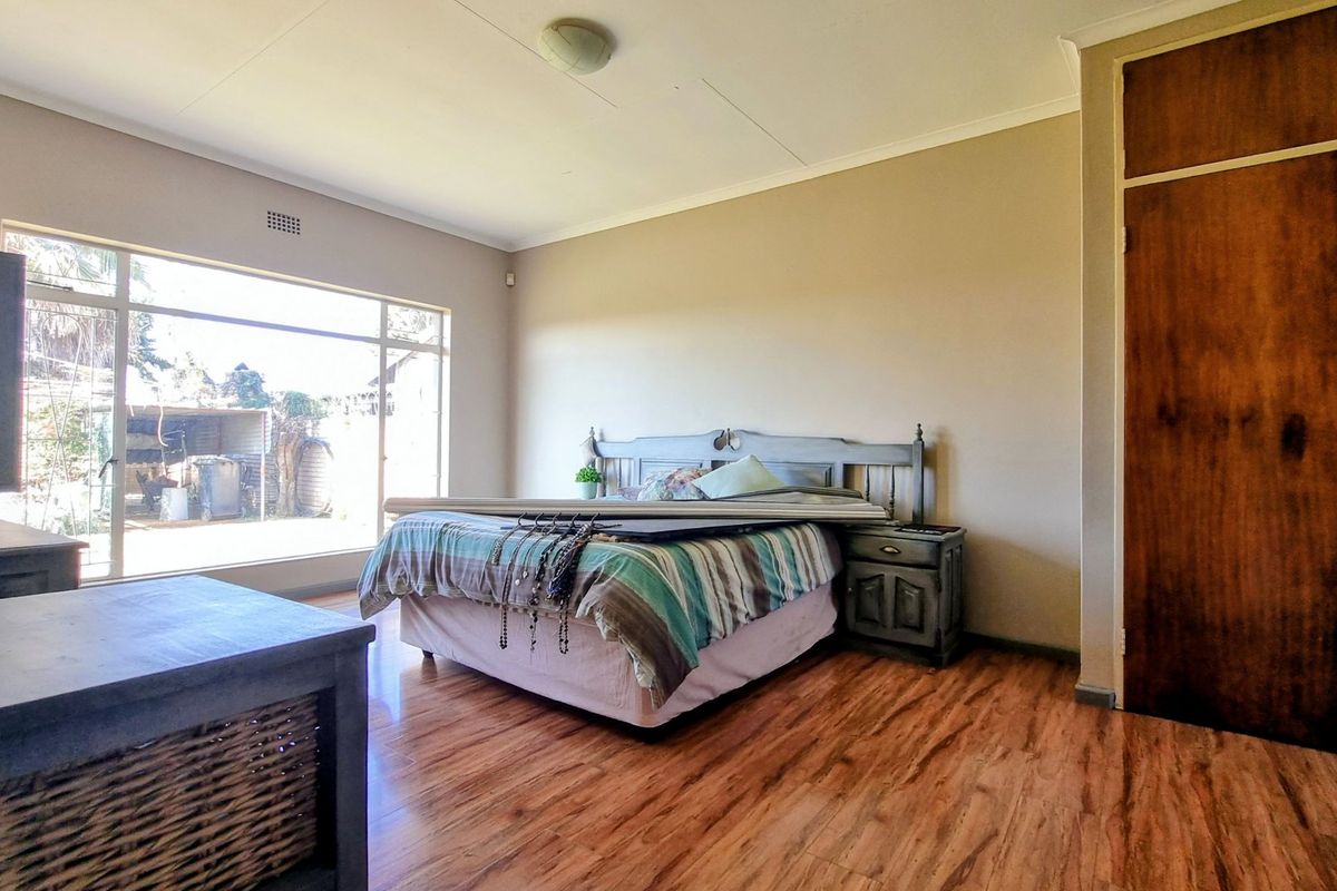 A spacious bedroom featuring laminate flooring, a large window providing natural light, and a built-in wooden wardrobe.
