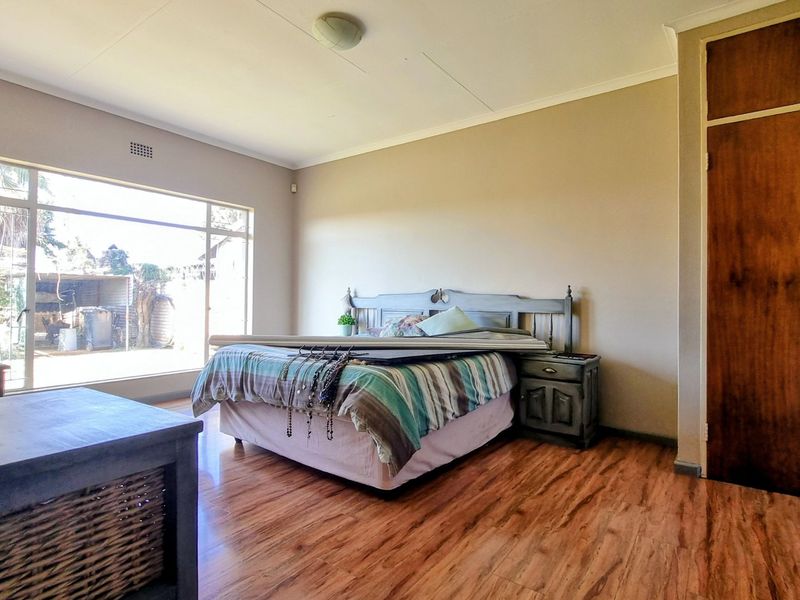 A spacious bedroom featuring laminate flooring, a large window providing natural light, and a built-in wooden wardrobe.