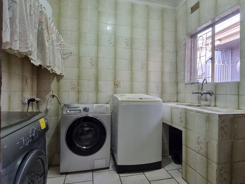 Functional laundry room featuring tiled walls, a built-in sink, and dedicated space for multiple washing machines.