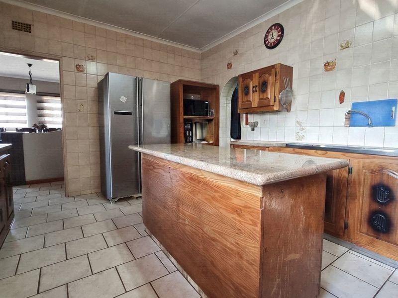 A functional kitchen featuring wooden cabinetry, granite countertops, a central island, and tiled finishes throughout, offering a classic layout with potential for modernization.