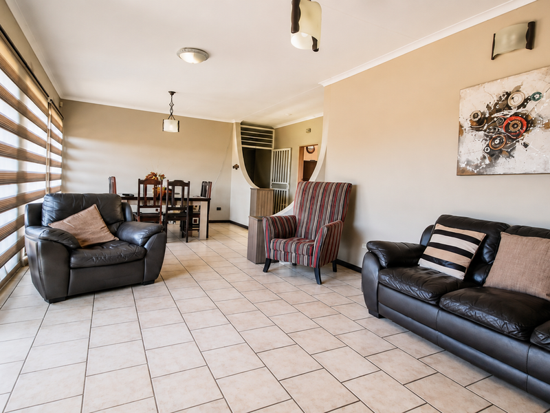 Spacious open-plan living and dining area featuring neutral tiled flooring, large sliding doors for natural light, and integrated ceiling and wall lighting.