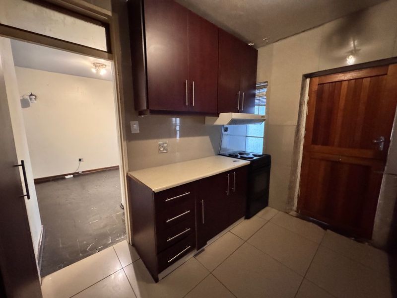 A compact kitchen featuring dark wood cabinetry, tiled flooring, and a freestanding stove, requiring minor cosmetic updates to improve the overall finish.