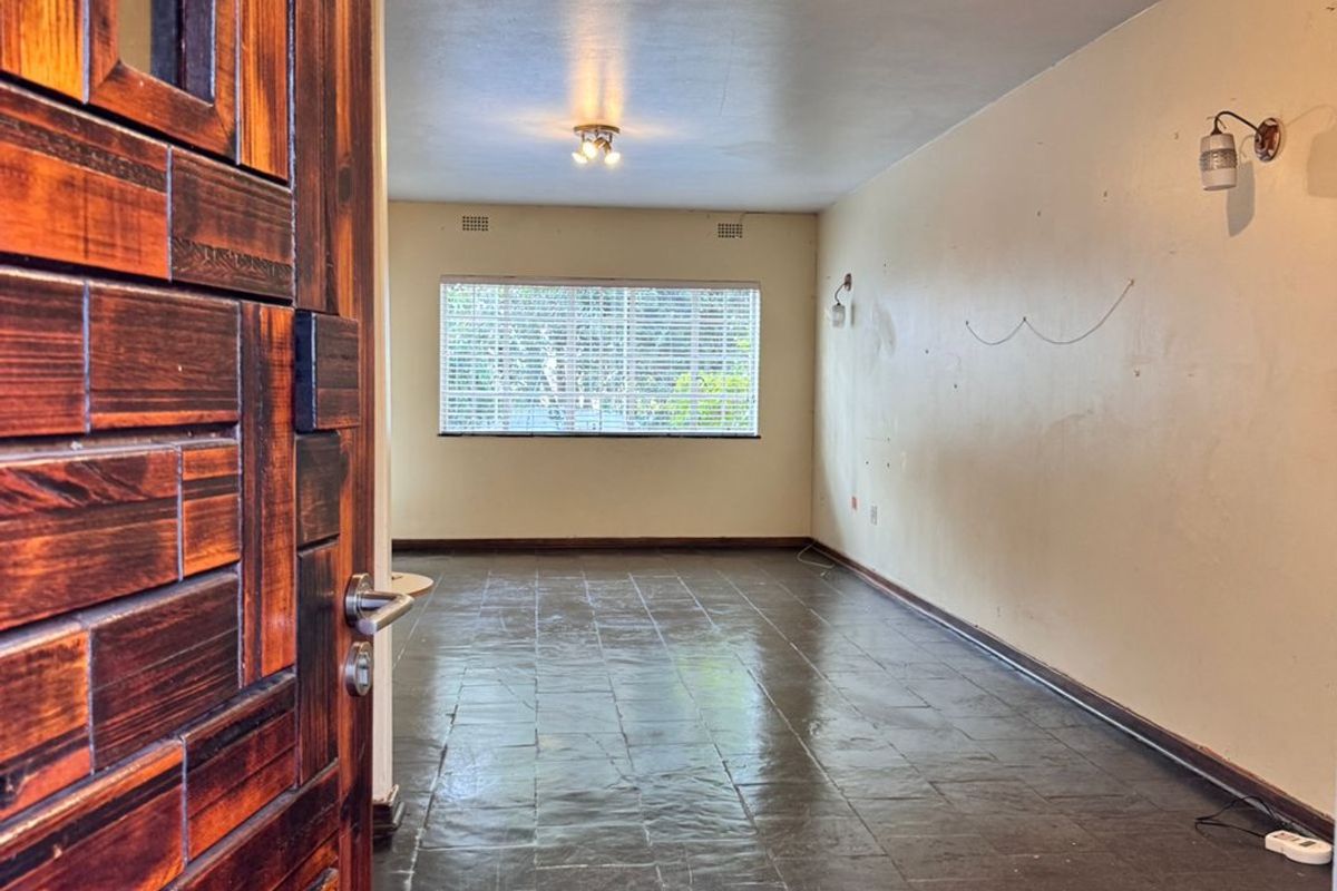 An empty, open-plan living area featuring dark tiled flooring, wall sconces, and a solid wood entrance door, ready for personalization.