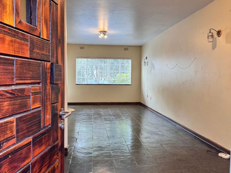 An empty, open-plan living area featuring dark tiled flooring, wall sconces, and a solid wood entrance door, ready for personalization.