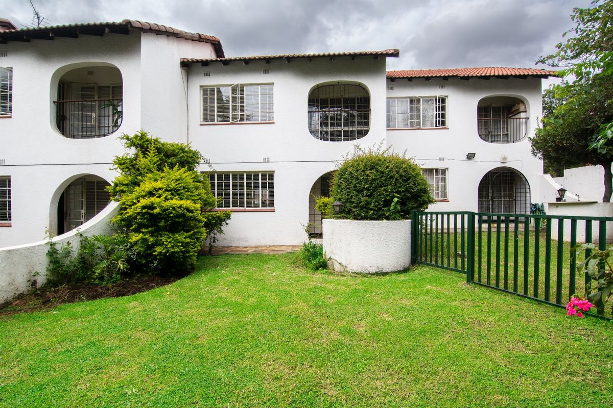Rear view of a multi-story apartment building featuring white textured facade, terracotta roof tiles, and a private garden area with metal fencing.