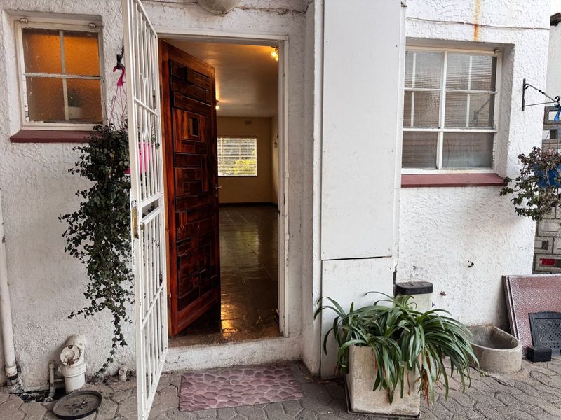 Exterior view of an apartment entrance featuring a security gate, timber door, and tiled flooring visible through the open doorway.