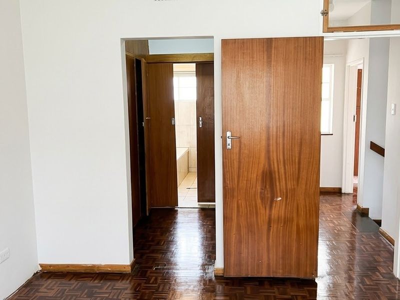 An empty bedroom featuring classic parquet flooring, wooden doors, and a transom window, providing a neutral canvas for interior design updates.