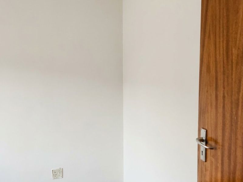 A clean, empty bedroom corner featuring well-maintained parquet flooring and a solid wood door.