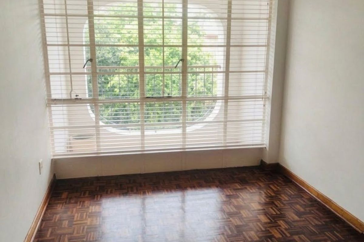 A bright, empty bedroom featuring classic parquet flooring, large window with security bars, and fitted venetian blinds.
