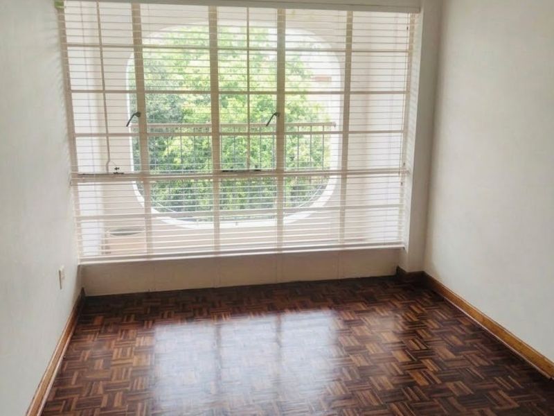 A bright, empty bedroom featuring classic parquet flooring, large window with security bars, and fitted venetian blinds.