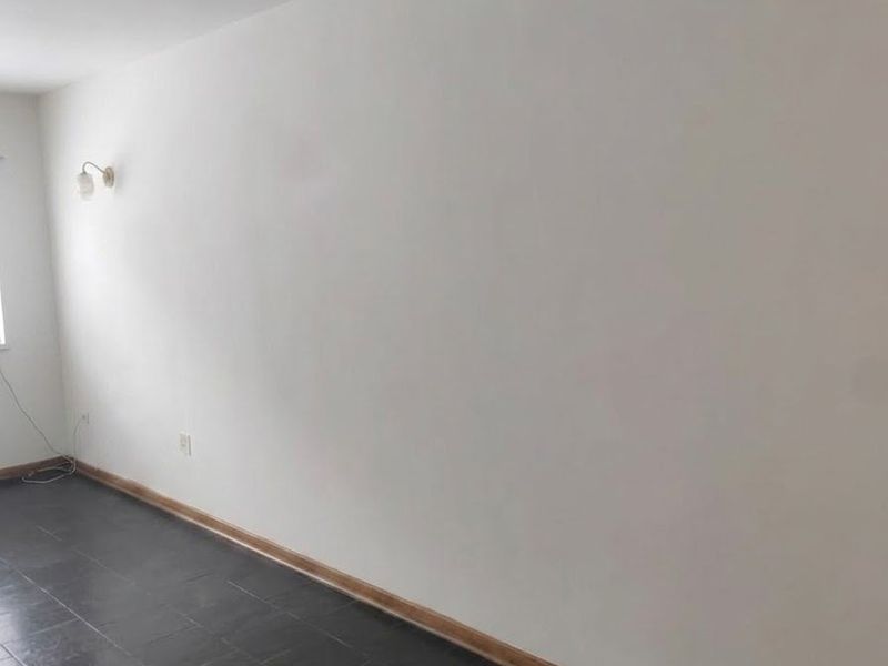 An empty living area featuring dark slate tile flooring, wooden skirting boards, and a wall-mounted light fixture.