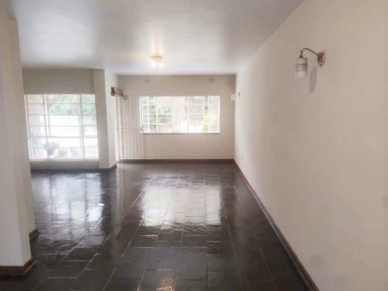 A spacious, empty living area featuring dark tiled flooring, large windows for natural light, and wall-mounted lighting fixtures.
