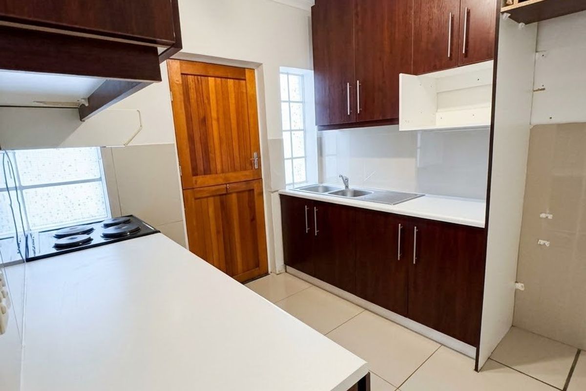 A functional kitchen featuring dark wood cabinetry, a built-in electric hob, stainless steel sink, and tiled flooring, offering a clean and practical workspace.