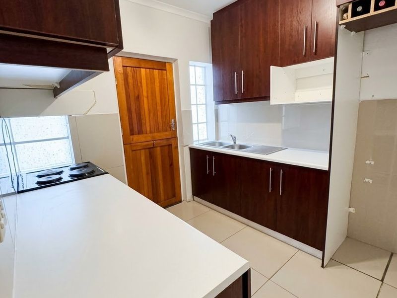 A functional kitchen featuring dark wood cabinetry, a built-in electric hob, stainless steel sink, and tiled flooring, offering a clean and practical workspace.
