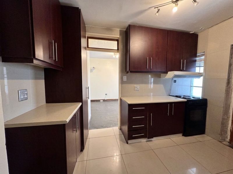 A functional kitchen featuring dark wood cabinetry, stone countertops, tiled splashbacks, and ceramic flooring, offering a clean and practical workspace.