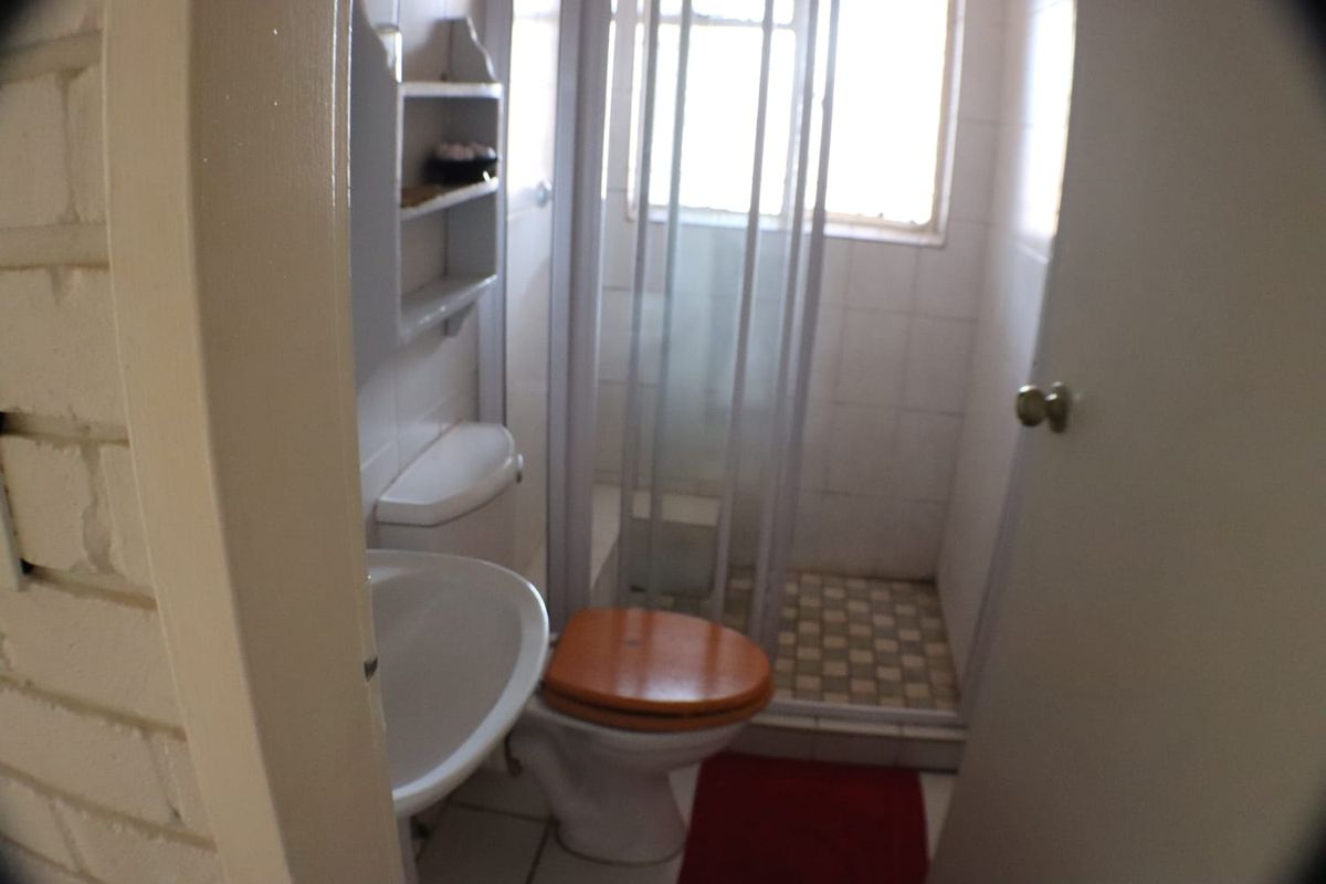 A compact bathroom featuring a shower enclosure, pedestal basin, and toilet with tiled finishes, requiring modernization to improve its overall condition and appeal.