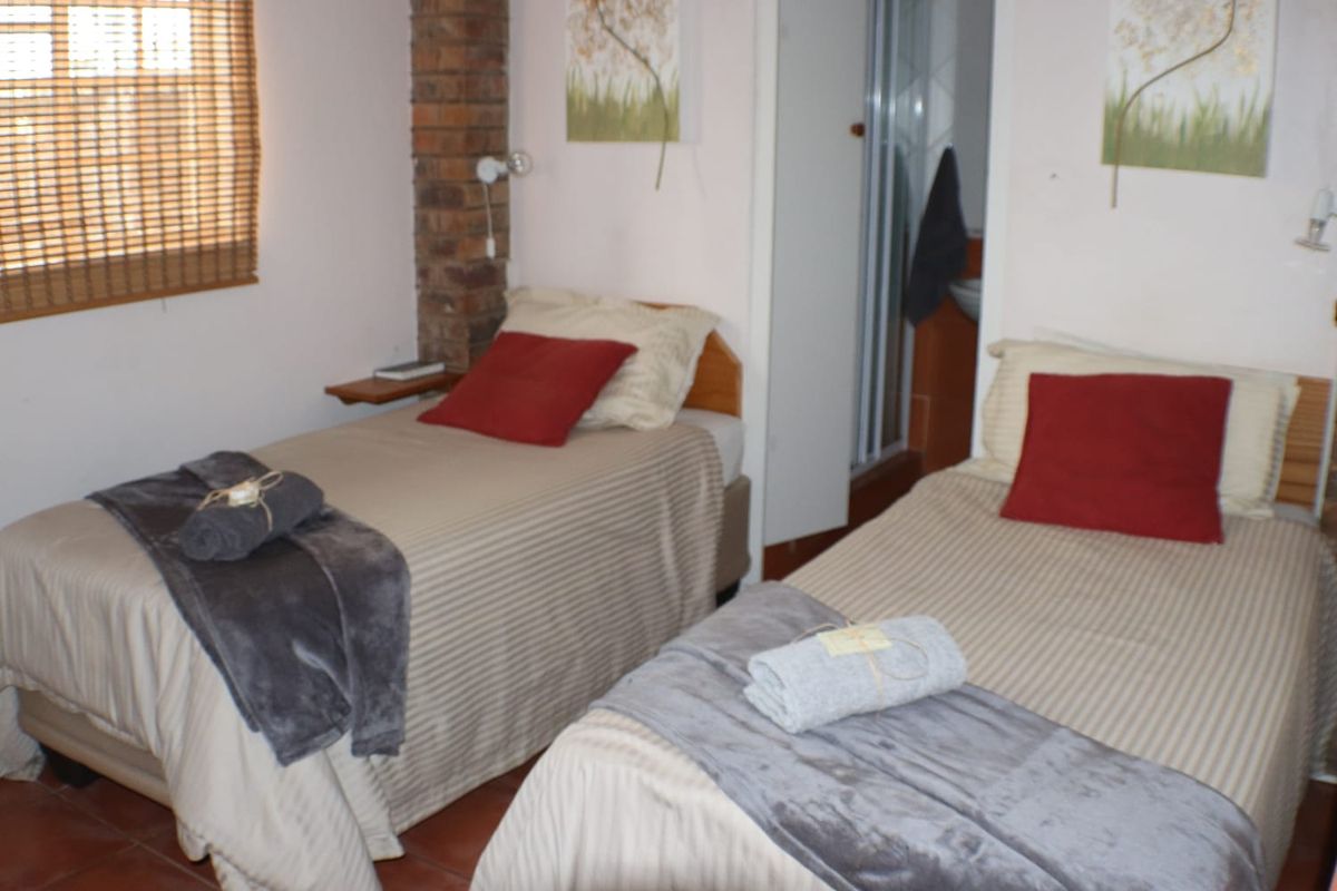 A bedroom featuring an exposed brick pillar, tiled flooring, and a bamboo blind, with an adjacent en-suite bathroom area.