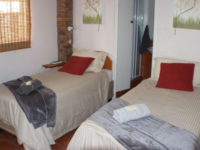 A bedroom featuring an exposed brick pillar, tiled flooring, and a bamboo blind, with an adjacent en-suite bathroom area.