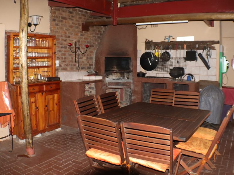 Covered outdoor entertainment area featuring a built-in braai, exposed brickwork, timber beam ceiling, and durable brick flooring, ideal for social gatherings.