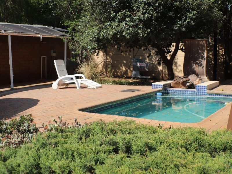 Outdoor pool area featuring a paved deck, covered patio space, and a built-in water feature, surrounded by established garden greenery.