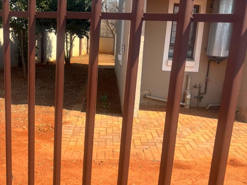 View of the rear exterior area featuring a paved walkway, external geyser, and metal security fencing.