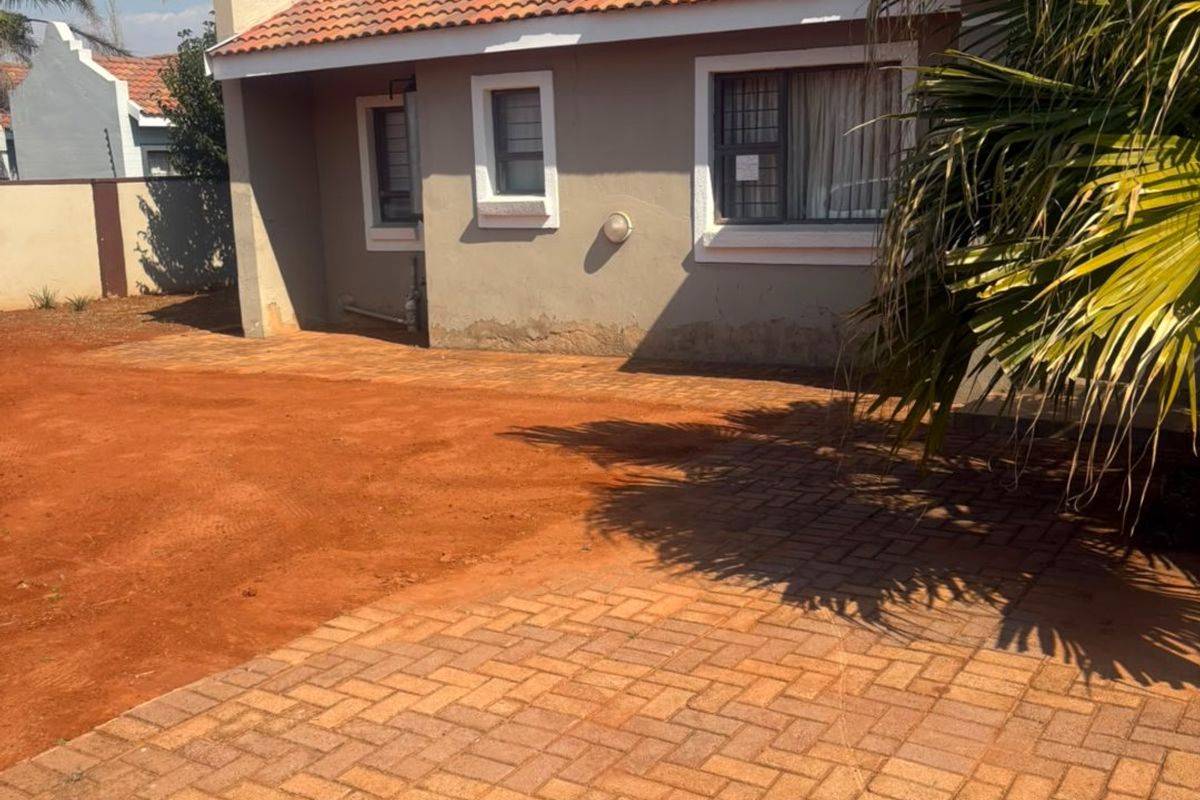 Rear exterior view of the house featuring a paved driveway, terracotta tiled roof, and boundary walling.