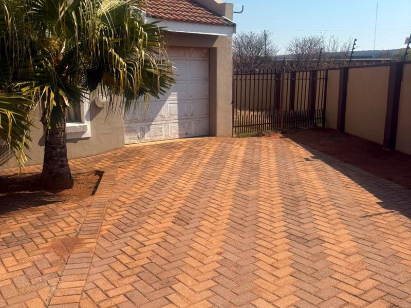 Front exterior view featuring a paved driveway, garage access, and secure perimeter fencing.