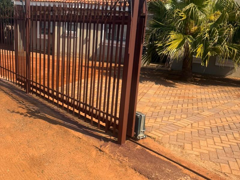 Front view of the property featuring a secure sliding gate with an electric fence, paved driveway, and a tiled roof structure.